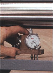 The planer bead gauge has to work in different positions. The base screw can straddle the bed slots. To check the feed rollers, orient the dial indicator, so it can take overhead reading. To check the bed rollers (shown here), flip the indicator on the tool post, sticking the plunger down through the hole in the base. 