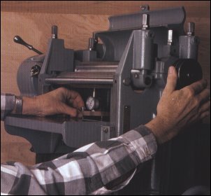 The bed gauge checks infeed and outfeed components. It also shows if bed adjustments are needed. By turning the pulley, the author rocks the cutterhead to be sure that he is reading bottom dead center of the arc of the knives. 